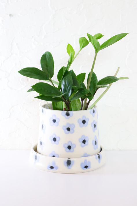 Dress up your houseplant in these handmade planters. Opening is ideal for a 4” nursery pot. Each plant home features a drainage hole, and matching saucer. Lovingly handmade in Portland, Oregon. Perwinkle flowers adorn a white clay body. Ceramic Pot Design, Ceramic Pot Design Ideas, Flower Painted Pottery, Plant Ceramics, Ceramic Design Ideas, Plant Pot Designs, Plant Pot Painting Ideas, Nursery Pottery, Plant Pot Painting