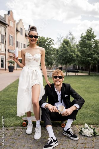 Stock Image: happy interracial couple, wedding attire, sunglasses, with french fries, looking at camera in city Grunge Engagement Photos, Formal Couple Poses, Engagement Shoot Ideas Unique, Retro Couple Photoshoot, Interracial Couple Wedding, Engagement Editorial, Retro Engagement Photos, Smaller Wedding, Dance Couple