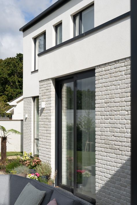 This project involved the complete remodelling and extension of an existing two-story dwelling to create new, integrated facades and a flexible floor plan for a modern family. The design combines modern details and materials with traditional shapes, featuring a contemporary dormer roof. Extra floor space was added to the rear, with first-floor extensions and a new roof enhancing the house's street view. The ground floor footprint was retained, extending the first floor west and rearward. A cantilevered entrance canopy with planters and rainscreen modernises the exterior. The rear elevation includes a contemporary brick and render and two flat-roofed volumes with large glazed openings. The first floor extends westward, maintaining the linear rhythm of the front and back elevations. Brick Extension, Rendered Houses, Dormer Roof, Rear Elevation, Modern Bungalow House, New Roof, Modern Bungalow, Bungalow House, House Extensions