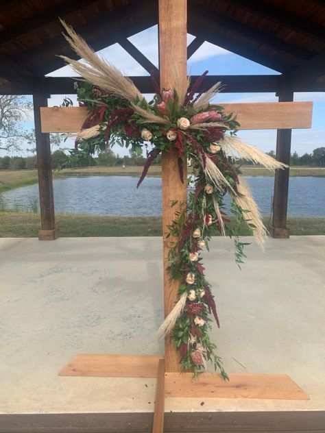 A combination of beatiful burgandy and blush florals combined with the trendy pampas grass softens the beatiful wooden wedding Cross for the picture perfect wedding Boho Wedding Cross Decor, Diy Cross For Wedding, Cross Backdrop For Wedding, Decorated Cross For Wedding, Cross Floral Arrangements Wedding, Cross Arbor Wedding, Wedding Cross Altar, Wooden Cross Wedding, Cross Wedding Backdrop