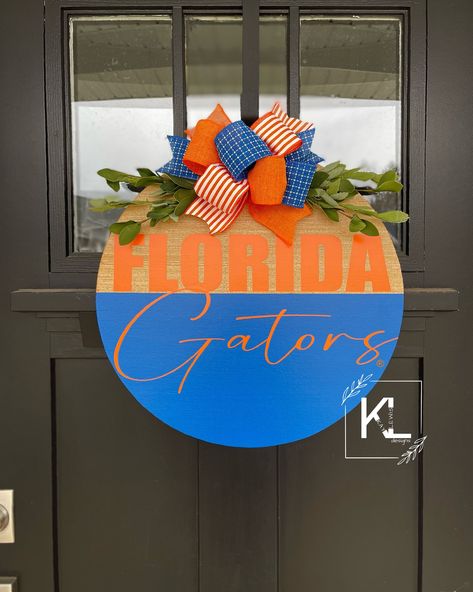 "*OFFICIALLY LICENSED COLLEGIATE PRODUCT* Florida Gators Door Wreath | Front Door Decor | Gators Door Hanger | Front Door Wreath | Florida Gators Football | Florida Gators Decor Now available in 3 sizes - 16\", 18\", & 20\" Comes ready to hang with twine wire attached! One coat of poly acrylic applied! Bow and greenery attached! (NO glue used) All signs are handmade from myself and my husband!  Please be aware there will be small imperfections and wood markings. I strive for perfection and want to do my best to ensure you get the best quality from me.  Please be aware that greenery and bows may vary depending on stock.  Colors and greenery will be similar to what it shown. ALSO, any word/text/fonts can be changed prior to purchase.  Just send me a message.  Contact me for any custom orders How To Attach Twine To Door Hanger, Florida Gators Football, Word Text, Gators Football, Florida Gator, Florida Design, Room Theme, Front Porch Signs, Door Entry