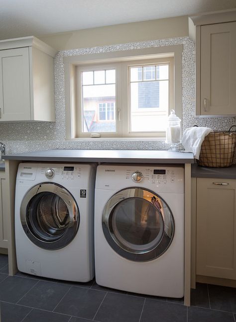 Fabulous laundry room features tan cabinets paired with gray quartz countertops and white mosaic bubble tiles and an enclosed washer and dryer tucked under windows accented with tan moldings alongside late tiled floors. Tan Cabinets, Hardwood Floors In Bathroom, Gray Quartz Countertops, Laundry Room Folding Table, Transitional Laundry Room, Laundry Pantry, Grey Laundry Rooms, Gray Quartz, Laundry Ideas