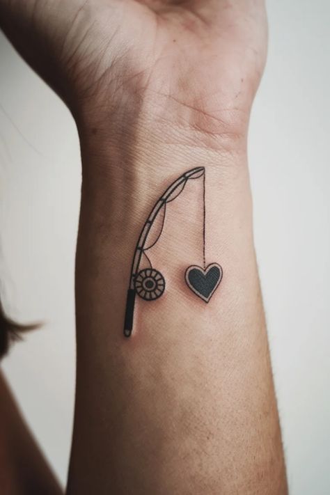 Fishing rod tattoo with line and heart-shaped lure on forearm. Fishing Related Tattoos, Fishing Lure Tattoo Women, Small Fish Tattoo For Women, Simple Fishing Pole Tattoo, Bass Fish Tattoo Women, String Tattoo Ideas, Fisherman Tattoo Ideas, Small Fishing Tattoo, Fishing Boat Tattoo