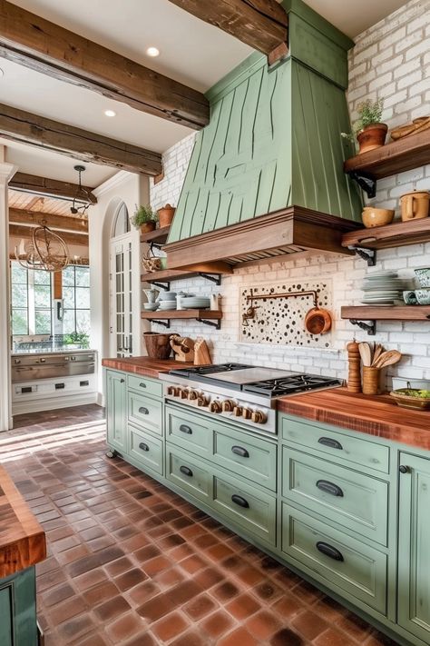 Farmhouse Elegance | Sage green cabinetry with a distressed finish • Rich terracotta brick flooring in a herringbone pattern • Exposed dark wooden ceiling beams • Textured white brick backsplash • Natural wood open shelving adorned with terracotta pots and white dishes • Oversized green range hood with shiplap detailing • Elegant arched white window • Vintage-inspired hanging copper pots • Warm ambient lighting and earthy tones create a cozy, traditional kitchen space. Green Range Hood, Rustic Kitchen Green, Green Aesthetic Home Decor, Green Aesthetic Home, Kitchen Exposed Brick, White Brick Backsplash, French Country Kitchen Ideas, Petite Kitchen, French Country Kitchen Designs