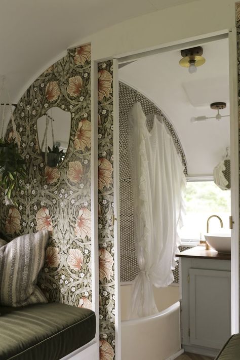 Interior photograph of a vintage Airstream travel trailer. Floral wallpaper, velvet sofa in the bedroom, a sink, brass faucet, and penny tile in the bathroom. Garden Caravan, Remodel Camper, Modern Caravan, Camper Vintage, Rv Bedroom, Rv Dreams, Modern Bunk Beds, Airstream Remodel, Airstream Interior