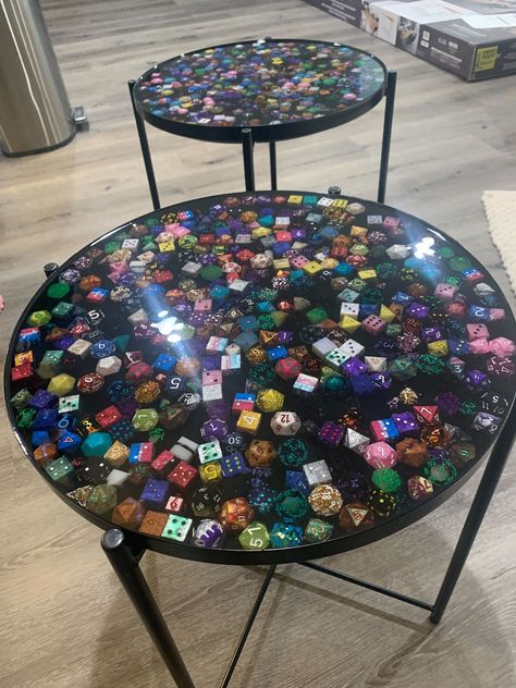 We use GLADOM Tray Table from Ikea and fill them with handmade and painted dice. We place the dice in the tray then pour a clear layer of epoxy over it to ensure each die can be seen. These tables are water resistant and beautiful!  This process requires around 200 dice and nearly an additional gallon of epoxy! Pokemon Resin Table, Dice Furniture, Epoxy Tray Ideas, D&d Room, Geek Living Room, Gladom Tray Table, Men Furniture, Dice Display, Dice Table