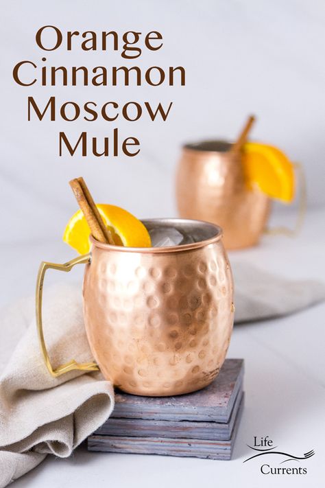 Two Moscow Mule drinks in copper mugs the front one is on a stack of grey tiles with a grey linen napkin and a title Spicy Ginger Simple Syrup, Cinnamon Vodka Cocktails, Orange Moscow Mule Recipe, Apple Cider Moscow Mule, Cinnamon Cocktail, Moscow Mule Drink, Cinnamon Simple Syrup, Orange And Cinnamon, Spicy Drinks