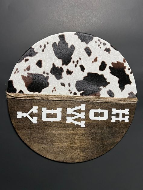 Enhance your country home decor with our Rustic Roots Decor Howdy Door Hanger. This charming piece features a 14.0 inch wooden round, half of which is stained with the color of your choice, while the other half boasts a stunning cow faux leather design. The center is then wrapped with twine for added texture and visual appeal. Featuring a bold classic county font in bright white, this Howdy Door Hanger adds an inviting touch to any space. Hang it on your front door to welcome visitors or place it indoors as part of your rustic decor. The high-quality construction ensures that this door hanger will last for years to come and make an impression on anyone who sees it. Get ready to receive compliments from friends and family alike when you display our Rustic Roots Decor Howdy Door Hanger in yo Cow Print Door Sign, Cow Print Front Door Sign, Cow Print Decor, Cow Front Door Sign, Cow Print Wood Sign, Western Door, Cow Door Hanger Metal, Round Signs, Christmas Craft Show