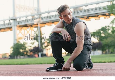 Young man on sports track, kneeling, looking away - Stock Image Man Crouched Down Reference, Man Squatting Pose, Kneeling Pose Reference Front View, Crouched Pose Reference Drawing, On One Knee Pose Reference, Guy Kneeling Pose, Man Kneeling Pose Reference, Person Crouching Reference, Guy Kneeling