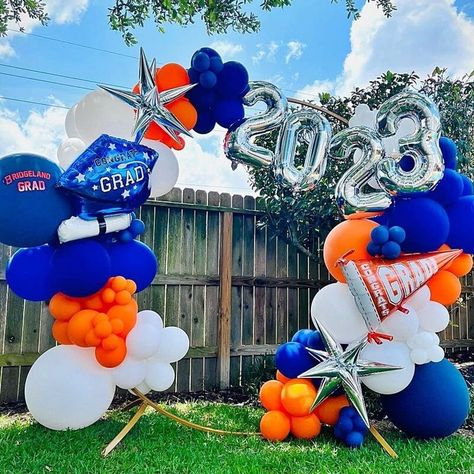 Celebrate your academic milestone by creating a vibrant balloon arch. Use a mix of matte white, royal blue, and orange latex balloons in varying sizes to create depth. Add some silver number mylar foils to spell the year you graduated and get some starburst cone balloons. Tie all these together to a round metal arch backdrop stand where your family and friends can take amazing photos. Blue And Orange Balloon Arch, Graduation Balloon Arch, Balloon Boutique, Metal Arch Backdrop, Balloon Graduation, Royal Blue And Orange, Event Decor Ideas, Arch Backdrop Stand, Party Decorations Table