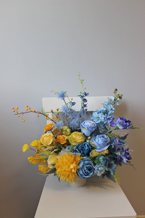 Adorn your table with the radiant charm of our blue and yellow centerpiece, a splendid addition perfect for weddings or a delightful springtime affair. This silk flower arrangement, carefully crafted to capture the essence of the season, exudes a vibrant and refreshing aura. With a harmonious blend of blue and yellow hues, this centerpiece illuminates any setting, bringing forth a cheerful and inviting atmosphere. Its captivating design not only serves as a focal point but also infuses the space Blue Yellow Decorations Party, Blue Arrangements Flower, Blue And Yellow Flower Arrangements, Yellow And Blue Wedding Flowers, Blue And Yellow Wedding Flowers, Yellow And Blue Wedding, Yellow Centerpiece, Yellow Wedding Decorations, Yellow Flower Arrangements