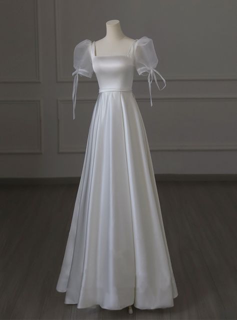 Bidding farewell to conventional wedding attire, this wedding dress introduces a blend of modernity and classic charm. The satin fabric ensures a smooth, lustrous finish that gracefully flows with every step. The dress features delicate puff sleeves tied with elegant bows, adding a touch of whimsy and romance. Its square neckline and fitted bodice create a timeless silhouette, while the A-line skirt flows effortlessly to the floor, making it perfect for twirling on the dance floor. The high-qual Square Neckline Dress Prom, Elegant White Long Dress, Classic Dance Dress, Narnia Inspired Wedding Dress, Wedding Satin Dress With Sleeves, Princess Dresses White, Small Wedding Wedding Dress, Wedding Dress Dance Party, Poof Sleeve Wedding Gown