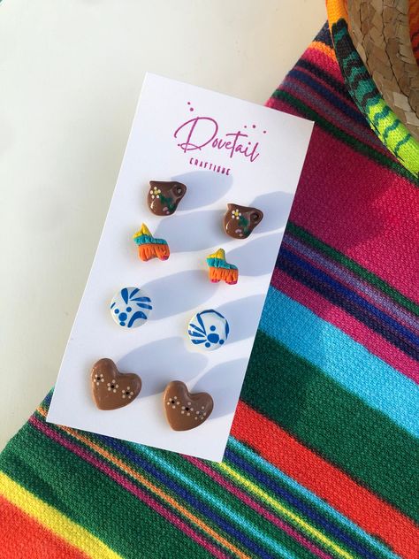 Looking for cute Latino-inspired polymer clay earrings? Grab this four-pack of mini studs that scream "Soy Latina!" Handmade here in the Alamo City, these Mexican-style stud earrings are perfect for a fiesta! You get all four flatback earring sets! This set includes glazed barro pottery jarritos, colorful fiesta piñatas (colors vary), glazed cazuelita style barro pottery heart studs, and classic talavera patterned round studs. Lightweight and colorful, these earrings are petite (see measurements) making them great for those looking for adorable interchangeable pairs or those with multiple piercings. They are also great for giving as a gift or sharing with a friend! Each set is secured to steel silver-toned posts with UV resin, making them long-lasting. All earrings are made of quality FIMO Mexican Clay Earrings, Frida Kahlo Party Decoration, Mexican Party Favors, Talavera Pattern, Unique Hair Bows, Pottery Heart, Charm Bar, Diy Gifts To Sell, Resin Making