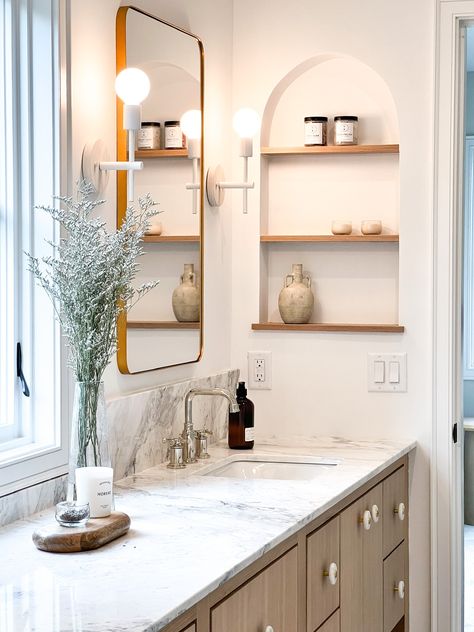 This bathroom has all the most beautiful design features! From the marble countertop and backsplash, the oak vanity and unique knobs, to the arched niche with shelves built into the wall, it truly is impressive!    New Construction | Home Trends 2024 | Home Design | Minnesota Home Trends Arch Niche Bathroom, Built In Niche Bathroom, Arched Niche In Wall Bathroom, Bathroom Vanity Niche, Niche With Shelves, Vanity Niche, Arched Niche In Wall, Recessed Shelves Bathroom, Niche In Wall