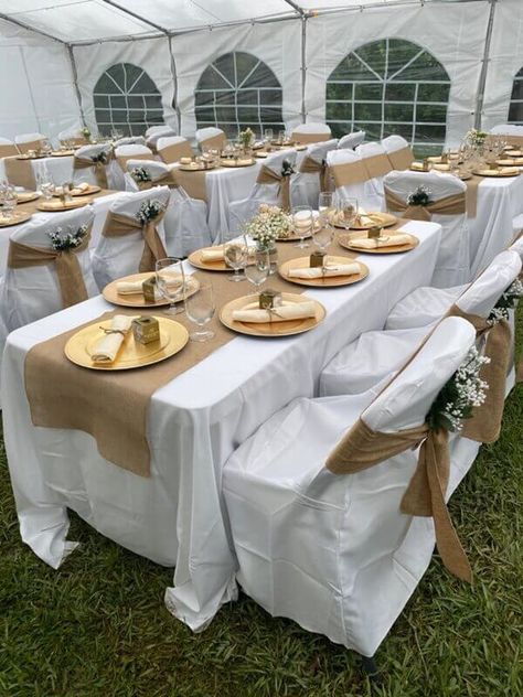 Exude rustic vibes with your outdoor wedding décor setup by dressing up your tables with white tablecloths and burlap runners. Also, cover your chairs with white chair covers along with burlap chair sashes and tuck in white baby breath florals for an ethereal touch. Wow your guests with an impressive place setting using gold chargers, burlap napkins, and favor boxes. Moreover, add gorgeous visual appeal to your arrangement by arranging alluring florals in glass vases as your table centerpieces. Table Runners Gold, Brown And White Centerpieces, White Table Cloth With Gold Runner, Rustic Wedding Table Set Up, Burlap Table Settings, Chair Covers Wedding Reception, Outdoor Events Decor, Outdoor Night Wedding, Burlap Chair Sashes