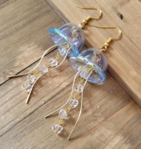 18k gold plated stainless steel handmade earrings of light blue aura jellyfish. These Jellyfish are made from dainty blue iridescent acrylic domes, glass crystal studded chain, and gold wisp tendrils.  The difference between these earrings and my popular Jellyfish earrings are the domes- unlike my green, teal, pink, and purple ones, these domes are made from a hard plastic so they are less fragile, and can be coated in the rainbow iridescent aura that is color shift depending on lighting and angle.  Please note that these earrings jingle similarly to my glass Jellyfish earrings that dangle. They are not too loud, and make a really cute jingly sound as you move. If you are sensitive to earrings making sound as you wear, then these earrings may not be for you. Thank you for your understandin Jelly Fish Earrings Diy, Jelly Fish Earrings, Light Blue Aura, Jellyfish Accessories, Jellyfish Jewelry, Jellyfish Earrings, Iridescent Acrylic, Cool Earrings, Ocean Earrings