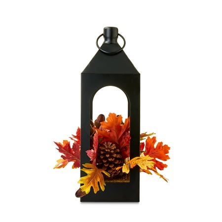 Create an enchanting and festive autumnal display with the Way To Celebrate Harvest Iron Lantern with Autumn Florals Tabletop Indoor Decor. This antique-style metal lantern is bursting with artificial fall florals like mini pumpkins, acorns, pinecones, and leaves. It is the perfect artificial floral arrangement for your fall and harvest season and is sure to blend in seamlessly with your existing decor, creating a cohesive decorating style. Nestle it amongst pumpkins, candles, and fall foliage on your dining room table for a gorgeous harvest centerpiece or place it on your mantel, coffee table, or end table as a stunning accent piece. Check out the entire Way To Celebrate collection for more harvest-inspired decorations and accessories including faux pumpkins, garland, decorative pillows, Fall Centerpieces, Fall Lantern Decor, Fall Party Decorations, Fall Lantern, Artificial Floral Arrangements, Iron Lanterns, Faux Pumpkins, Metal Lanterns, Harvest Season