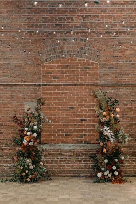 Wedding Brick Wall Decor, Brick Wall Floral Backdrop, Brick Wedding Ceremony, Fall Flower Installations, Exposed Brick Wedding Decor, Dried Flower Arch Wedding, Earth Tone Spring Wedding, Earth Tone Flower Arrangements, Brick Wall Wedding Backdrop