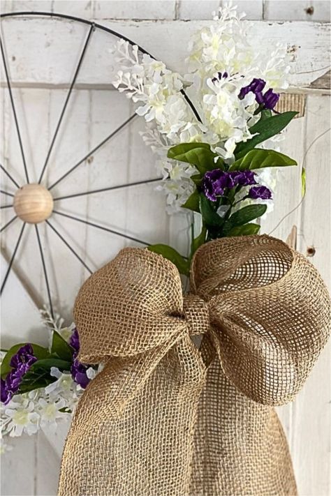 DIY Spring wreath made with a wagon wheel wreath form, white and purple flowers and a burlap bow.  The wreath is hanging on an old white door. Easy Spring Decor, Wagon Wheel Wreath, Wheel Wreath, Diy Decorating Ideas, Easy Diy Wreaths, Diy Spring Wreath, Diy Spring, Burlap Bows, Wreath Supplies