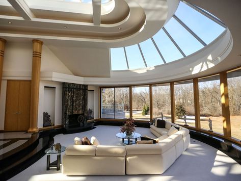 At the end of the long foyer, the wide, half-circle living room spreads out with a curved wall of windows under a curved ceiling of skylights. Windows On Curved Wall, Circle Skylight Architecture, Curved Wall With Windows, Curved Windows Living Room, Foyer Skylight, Curved Skylight, 2 Bedroom Loft House, Curved Walls Interior, Mall Stairs