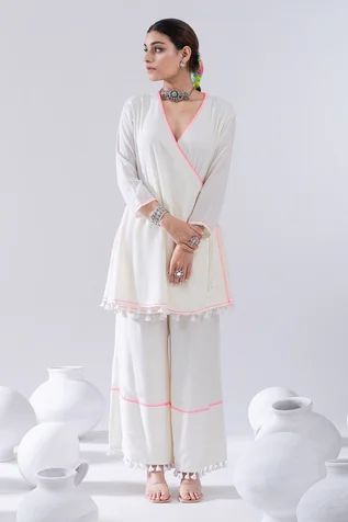 Ivory three quarter sleeve angrakha kurta, elevated with side tie-ups and pink thread embroidery. Paired with tassel laced palazzo. Component: 2 Pattern: Embroidery Type Of Work: Thread Embroidery Neckline: V Neck Sleeve Type: Three Quarter Sleeves Fabric: Cotton Voile Color: Ivory Other Details:  Tassel laced kurta Pink thread embroidery on palazzo Occasion: Puja,Sangeet - Aza Fashions Short Kurti With Palazzo, Palazzo Pants Outfit Indian, Angrakha Kurta, Kurta With Palazzo, Indian Kurti Designs, Angrakha Style, Beads Embroidery, Coord Set, Cotton Kurti Designs