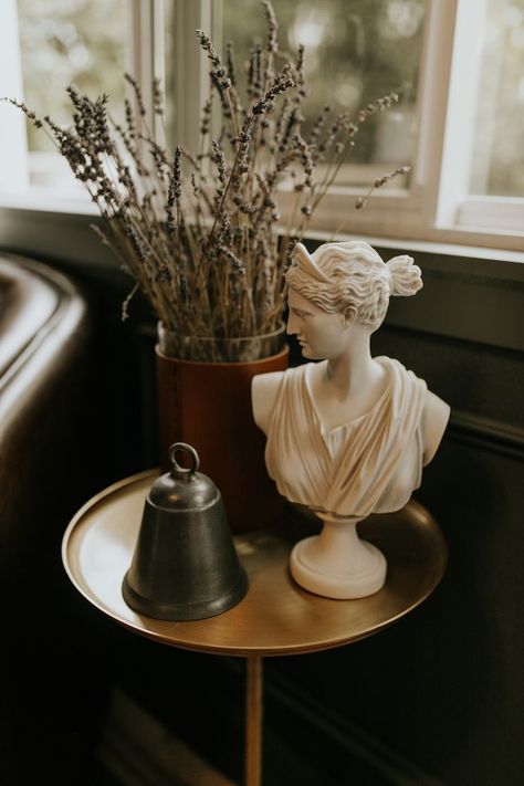 Bust sculpture, silver bell, dried lavendar, leather wrapped vase, gold side table Roman Bust Decor, Bust Statue Decor, Small Sculpture Ideas, Artifacts For Home Decor, Bust Decor, Greek Accessories, Roman Busts, Greek Decor, Gold Side Table