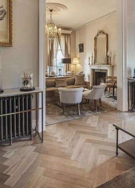 a sophisticated neutral space with light stained herringbone floors, neutral seating furniture, a fireplace and some lamps Family Room Flooring Ideas, Herringbone Entryway, Dark Herringbone Floor, White Stone Backsplash, Taupe Flooring, Curved Kitchen Island, Herringbone Floors, Parisian Bedroom, Herringbone Tile Floors