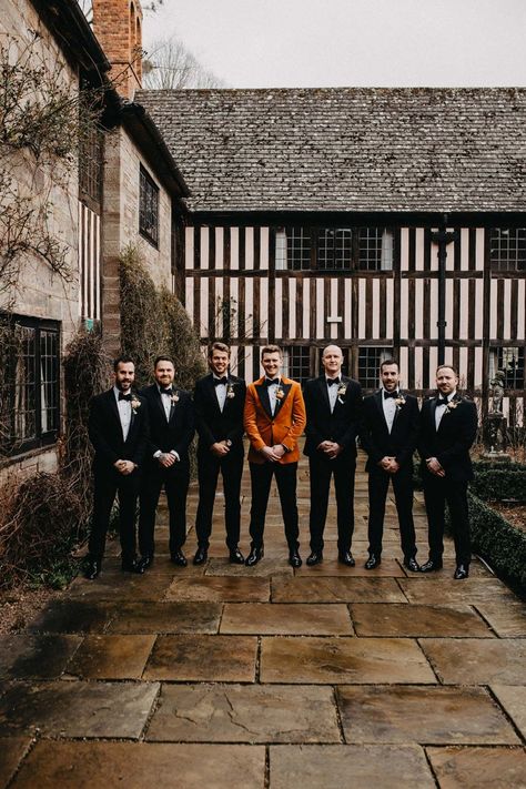 Groomsmen wearing classic black grooms suits with bowties standing with groom in crushed burnt orange velvet grooms blazer, black bowtie and black suit trousers outside Brinsop Court wedding venue | Jessica Grace Photography Black Wedding Dress Orange Bridesmaids, Black And Orange Tuxedo, Burnt Orange Bridesmaid Dresses With Groomsmen, Black Orange Wedding Theme, Rust Orange And Black Wedding, Black And Orange Fall Wedding, Burnt Orange Tuxedo Wedding, Black And Orange Wedding Theme, Burnt Orange Groomsmen Attire