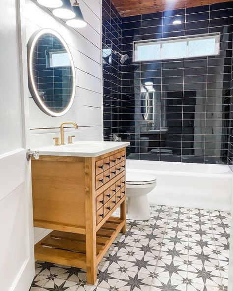 White frosted rectangular window is built into a glossy black tile shower over a white drop-in bathtub. A black round LED lit vanity mirror hangs from a white shiplap wall above a stained wood washstand with brass faucet. Black Tile Bathroom, White Subway Tile Shower, Black Tile Bathrooms, White Bathtub, Subway Tile Showers, Bathroom With Tub, Gray Shower Curtains, Drop In Bathtub, Pink Shower Curtains