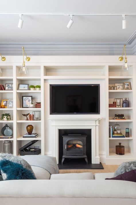 In our Bloomsbury project we wanted the wall mounted TV and the log burning stove to feel  very much part of the joinery unit
 
We created generous tall shelving units either side and continued this around and above the fireplace. 

The wooden fire surround is in the same colour as the lacquer units 

Fore more details and tips see our website Wooden Fire Surrounds, Log Burning Stoves, Joinery Design, Fire Surround, London Interior, Home Automation System, Shelving Units, Studio Interior, Library Design