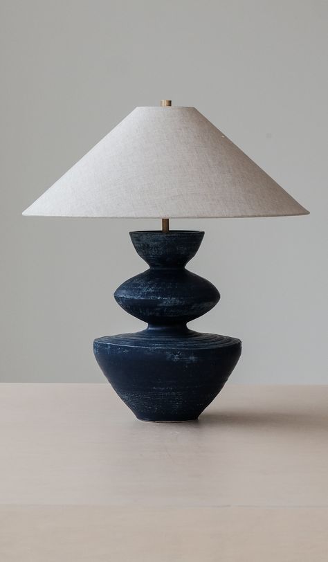 Handmade ceramic lamp base with conical oatmeal linen shade. Choice of satin 'anthracite' black (pictured), translucent 'stone' matte white (pictured), washy 'lapis' blue (pictured), crackle terra sigillata 'terrasig' white, matte 'ivy' green, matte 'chestnut' brown or metallic 'bronze' base finish. Approximately 23" tall including shade, 12" diameter ceramic base at widest point, 20" diameter shade. 10' 6" cotton cord with Pierre Krings prong plug. Takes (1) G16 shape, 60W max. incandescent bul Danny Kaplan Lamp, Table Lamp Blue, Handmade Ceramic Lamp, Clay Luminaries, Danny Kaplan, Blue Ceramic Lamp, Terra Sigillata, Ceramic Lamp Base, Ceramic Lamps