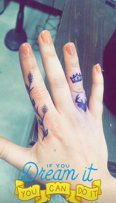 A woman's right hand extends out over a wooden table. Her nails are coral pink. She shows her finger tattoos. One on her index finger extending upward, a lavendar plant and flower. On her ring finger above the center knuckle is a crown, below the knuckle is a Stag with 6 points. Skin Art, Finger Tattoos, Family Crest, Tattoos, Skin, Art