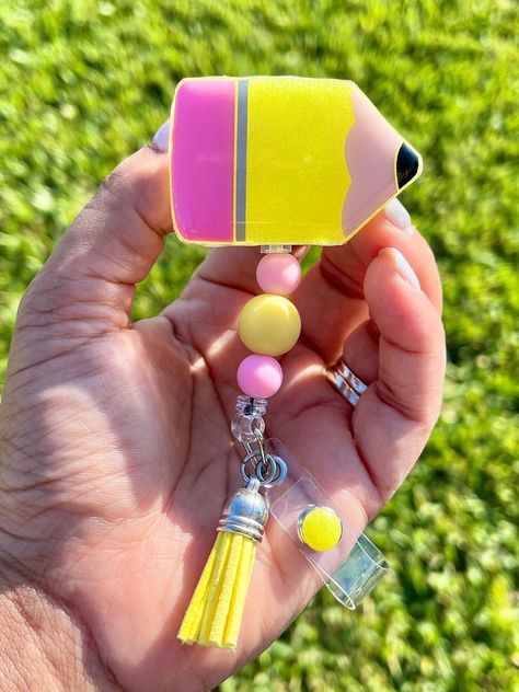 This Pencil Acrylic Badge Reel makes a perfect gift for teachers, paraprofessionals, or just anyone who wears a badge. It is handmade with a 2-inch acrylic piece with glitter and vinyl. It is then sealed with a clear coat of resin for a glossy clean look. Coordinating plastic beads, a tassel, and glittered resin on the snap are added to finish off the look. The badge is durable enough for everyday use.  Please keep in mind that every item is handmade; therefore, not every item will be the same b Teacher Badge Reel Ideas, Teacher Badge Ideas, Teacher Badge Reel, Badge Reels Diy, Teacher Badge Holder, Teacher Aesthetic, Teacher Accessories, Teacher Appreciation Gifts Diy, Teacher Craft