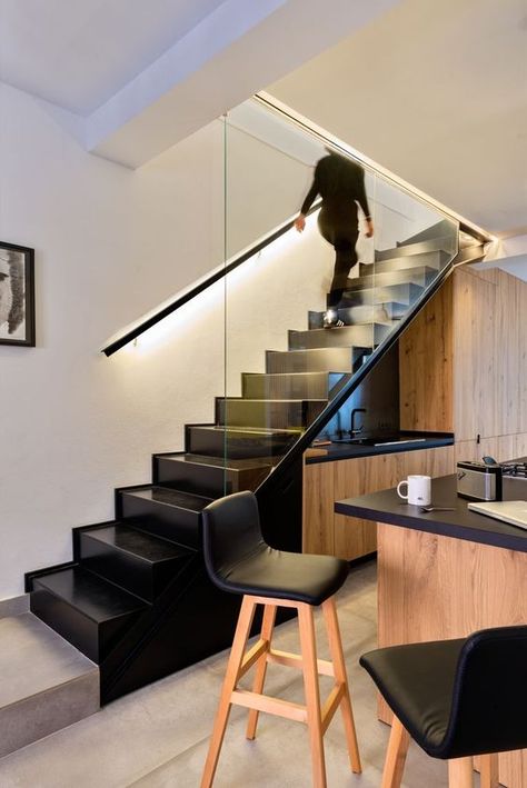 a stained kitchen built in under the staircase, with black countertops and lights, a matching kitchen island with black stools - DigsDigs Black Countertop And Backsplash, White Scandinavian Kitchen, Duplex Staircase, Kitchen Under Stairs, Black Modern Kitchen, Black Countertop, Stairs In Kitchen, Kitchen Built In, Timber Staircase