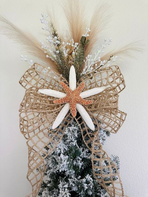 "This starfish tree topper will be the perfect addition to your family's beach holiday tree. Made with white 7-8\" starfish, sugar (orange) starfish, burlap net ribbon bow with 24\" tails (can be cut shorter), artificial pampas (does not shed), white glitter grass, and faux green seagrass.  This is a one-sided (180 degrees) tree topper. Need it to be double-sided? Order two! :) This topper will stick down into the top of your tree and  be able to be tied to the base of your tree with chenille st Seashell Tree Topper, Coastal Christmas Tree Toppers, Christmas Ocean Theme, Nautical Tree Topper, Starfish Tree Topper Diy, Beach Theme Tree, Coastal Christmas Tree Topper, Coastal Tree Topper, Beach Themed Christmas Tree