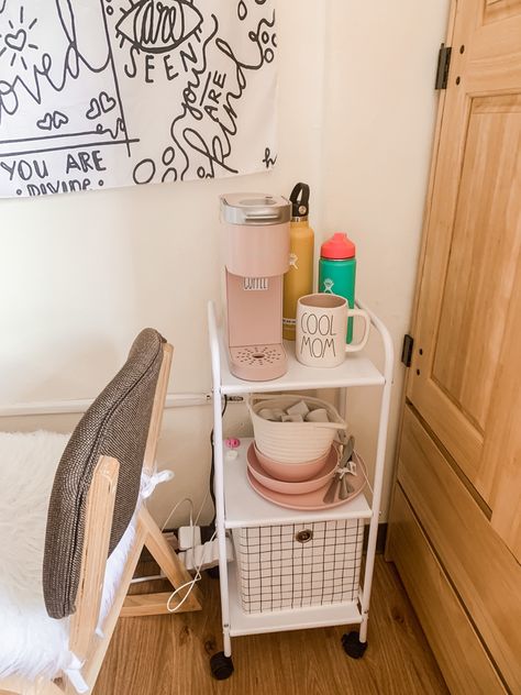 A white shelved small cart with a light pink keureg on top and a cool mom mug. On the second shelf are matching plates and a small basket with k-cups. On the bottom shelf is a checkered storage cube. College Coffee Station Dorm Room, Cheap College Dorm Room Ideas, Dorm Room Food Station, College Dorm Room Hacks Small Spaces, Coffee Cart Ideas Dorm, Coffee Station Dorm Room, College Dorm Room Ideas Storage, Dorm Room Layouts Triple, Dorm Cart Storage