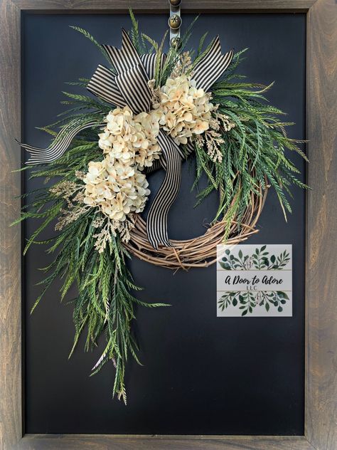 Beautiful everyday wreath to display all year around! This cascading beauty consists of cream hydrangeas, hanging greenery, and a beige and black bow. A different colored bow may be requested. This wreath measures around 30" from top to bottom tip.  This wreath is made to order and each one may have slight variations which make it unique.  A UV protectant is recommended in helping your wreath maintain its colors and quality. You can use the wreath indoors or outdoors, however a covered area/porc Black Door Wreath, Farmhouse Wreaths For Front Door, Hydrangea Wreath Summer, Front Door Baskets, Hanging Greenery, Diy Floral Wreath, Door Basket, Wreath Hydrangea, Silk Wreaths