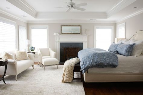 Elegant bedroom features tray ceiling accented with fan over pale gray walls framing windows flanking silver leaf mirror atop tall fireplace with millwork detail across from beige linen bed dressed in blue medallion bedding. Ceiling With Fan, Bedroom Tray Ceiling, Tray Ceiling Bedroom, Fitted Bedroom Furniture, Glamourous Bedroom, Bedroom With Sitting Area, Ceiling Fan Bedroom, Lillian August, Fitted Bedrooms