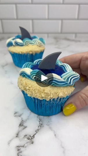 1.2M views · 9.7K reactions | You’re gonna need a bigger boat 🦈Would you take a bite of these shark week cupcakes that I made for Wilton Cake Decorating🦈🌊 Cut a curved sheet of parchment paper and stick it onto the top of the cupcakes, leaving a small gap at one side.🦈 Spread the sand-coloured buttercream over the gap.🌊 Crush up shortbread/graham crackers into sand and pour them over the buttercream.🦈 Peel off the parchment paper.🌊 Use an offset spatula to add some of the blue buttercream to the centre the other side of the cupcake.🦈 Add white, and two shades of blue buttercream to a piping bag, fitted with piping tip 32.🌊 Pipe a shell border around one side of the cupcake.🦈 Put them in the fridge for 20 minutes for the buttercream to set firm.🌊 Pour a small amount of blue jelly Underwater Cupcake Ideas, Scary Cupcakes, Aquarium Birthday, Shark Fin Cupcakes, Ocean Cupcakes, Beach Theme Cupcakes, Shark Cupcakes, Offset Spatula, Cake Techniques