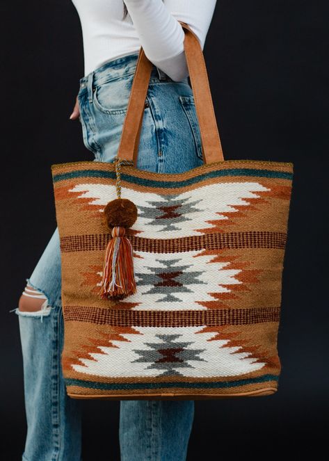 All our western lovers - this duffel is for you! Our restocked brown, rust, teal and cream Aztec inspired tote is a must have for all of your travels - big & small - this year!  Brown, rust and teal Aztec inspired tote Multicolored pom tassel detail Leather suede straps Measures 16" x 6" x 17" Designed in the U.S.A. Produced in India.  100% Cotton Lining: 100% Polyester Western Tote Bags, Gold Balayage, Fall Tote Bag, Fall Tote, Blouses Vintage, Flannel Sweatshirt, Bag Inspiration, Knitted Hats Kids, Into The West