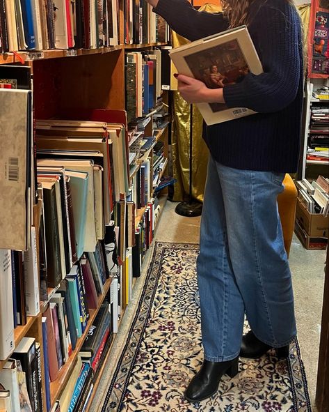 girl in blue jeans, blue sweater, and black boots with long brown hair looking at a bookcase full of old books in a cozy bookstore. bookstore full of pretty vintage books. cozy winter aesthetic. fall reading aesthetic. Bookstore Fall Aesthetic, Cozy Library Outfit, English Autumn Outfits, Bookstore Selfie, Cozy Pictures Aesthetic, Fall Inspo Board, Cool Fall Aesthetic, Bookseller Aesthetic Outfit, Lecturer Aesthetic