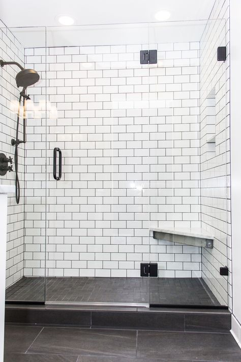 This shower create a beautiful contrast with white subway tile and dark gray/brown tiled floors. This shower includes frame-less glass shower doors, sloped shower with linear drain, a foot bench, and beautiful black shower fixtures. It's a perfect addition for a Portland bathroom.  #letsremodelpdx #interiordesign #bathroomremodel #portlandbathroom White Shower With Gray Floor, White Shower With Dark Floor, Subway Tile Bathroom Dark Floor, Minimalist Bathroom Ideas Small Spaces, White Tile Shower Gray Floor, Bathroom White Subway Tile Grey Floor, White Subway Tile Shower Ideas 3x6, Dark Grey Shower Floor Tile, White Subway Tiles Black Grout Bathroom