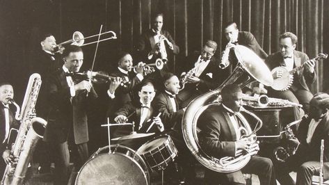 We see a band with some well-known instruments like drums and trombone. They make music that is called Jazz. It became very popular around the 1920s. The men wear neat suits. In the 1920s there were a lot of clubs, lounges and theaters in Chicago which played Jazz music, it was the new trend. It is believed that Jazz made its way through Chicago from New Orleans in 1915. Jazz is a mix of African and European musical traditions that started in the United States by african migrants form the west. 1920s Jazz, Violin Accessories, Jazz Players, Chicago History Museum, Electric Violin, Popular Bands, Jazz Artists, Jazz Club, Jazz Band