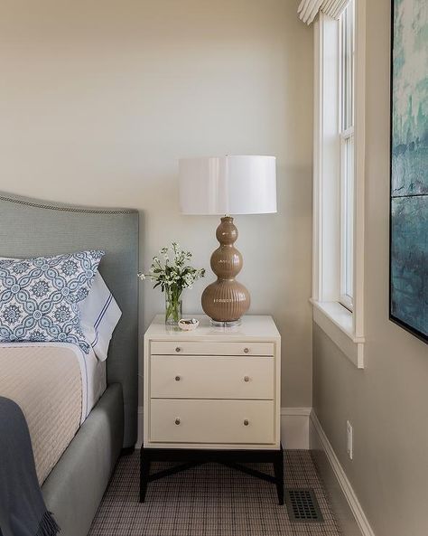 Elegant bedroom boasts a gray curved bed accented with silver nailhead trim dressed in a white and blue stitched sheet set next to a cream nightstand topped with a brown triple gourd rippled lamp. Edgecomb Gray Bedroom, Bm Edgecomb Gray, Transitional Design Bedroom, Neutral Bedroom Paint, Brown Lamp, Edgecomb Gray, Tranquil Bedroom, Transitional Bedroom, Neutral Paint Colors