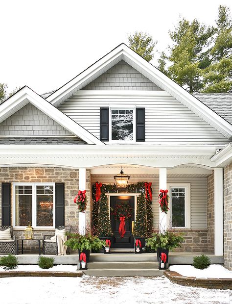 Christmas front porch decorated in classic greenery and red bows. House With Columns Christmas Decor, Decorate Front Of House For Christmas, Christmas Decorated House Exterior, Outdoor Traditional Christmas Decor, Outdoor Christmas Decorations Columns, Front Porch Christmas Decor Columns, Christmas Front Porch With Columns, Craftsman Christmas Porch, Front Porch Column Christmas Decor