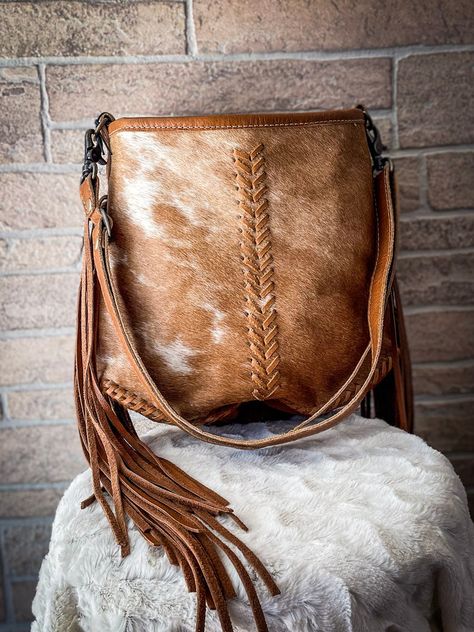 This shoulder bag is upcycled from cowhide. It has many inner compartments which makes it spacious. The combination of white and brown hairon along with the fringes gives it a very attractive look. Cowhide will vary. No two bags will be the same. You may or may not receive the image example shown.  Item Width 12 Item D Cowhide Diy, Outfit Accessories Ideas, Western Bags Purses, Western Bags, Myra Bags, Best Carry On Bag, Hay Bag, Western Bag, Cowhide Purse