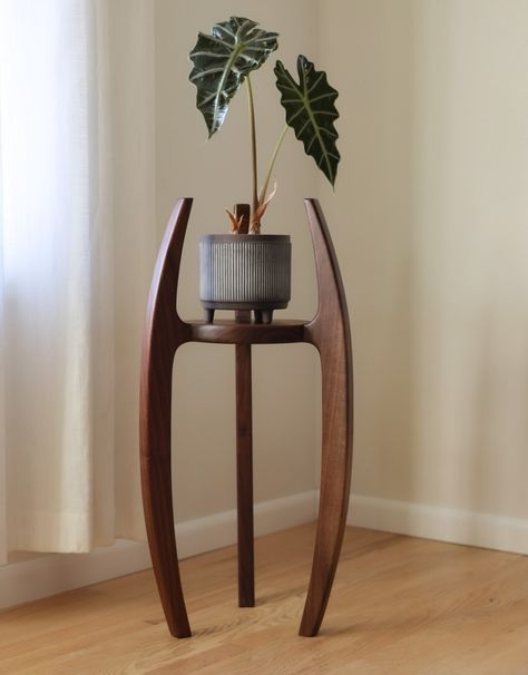 D E S C R I P T I O N This beautiful and elegant handmade plant stand evokes mid-century design with it's slightly tapered, curved legs. This premium quality stand is constructed of solid walnut wood using traditional joinery throughout for lifetime strength and durability.  Versatile feature: it has the option to be flipped so you can showcase your favorite potted plants high or low. Get your beloved plants off the floor and make a beautiful display of your green thumb with this charmer! Makes Plant Pillars Columns, Wood Pot Stand, Mid Century Modern Console Table Entryway, Wood Stand For Plants, Wood Plant Stands Diy, Mid Century Plant Pot, Art Deco Plant Stand, Wood Products That Sell, Plant Shelves Window