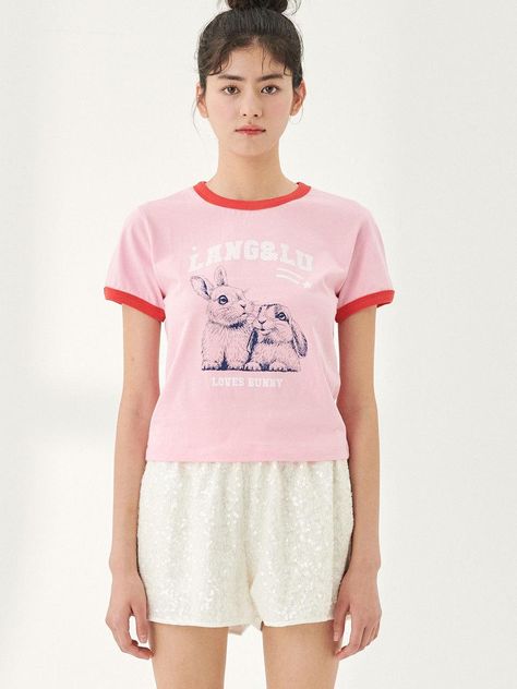 This t-shirt presents a playful and cute design, with a ringer style that includes contrasting trim on the collar and sleeve ends. On the front, there is a graphic of two bunnies and the brand name, along with the phrase LOVES BUNNY in a fun typeface. The graphic lends a whimsical and endearing quality to the shirt, which may appeal particularly to animal lovers or those who enjoy playful fashion. The shirt's overall design, with its short sleeves and comfortable fit, makes it a light and cheerful choice for casual wear.- The bunnies' detailed illustration is both charming and engaging, adding a soft, affectionate touch to the shirt's design.- Contrasting trims create a vintage-inspired look that's trendy and eye-catching.- The phrase LOVES BUNNY below the image adds a thematic message to 2 Bunnies, Two Bunnies, Playful Fashion, Bunny Graphic, Bunny T Shirt, Detailed Illustration, Love T Shirt, Cute Design, Animal Lovers