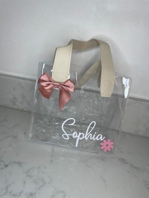 Beautiful clear PVC personalised gift bags with leather look double handles Perfect for a special birthday or celebration for a gift or party bag Size guide: 20 x 10 x 17 cm Personalised with any name Can also be changed to any other wording or message Font and colour of text can also be changed, and we have other colour options of the bow, if not noted at time of order then the pictured font will be used  ... daha fazla Clear Gift Bag Ideas, Clear Gift Bags, Plastic Gift Bags, Small Business Packaging Ideas, Custom Party Favors, Personalized Gift Bags, Wrapping Party, Party Gift Bags, Birthday Treats