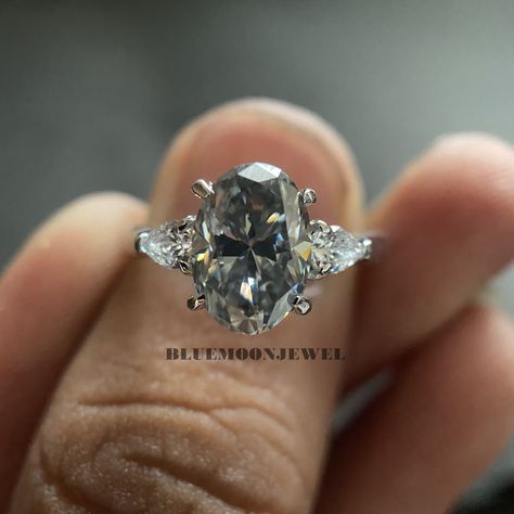 gray moissanite engagement ring, halo ring white gold, moissanite engagement ring vintage, moissanite engagement ring halo, engagement ring box, emerald engagement ring, emerald cut moissanite engagement ring, moissanite engagement ring vintage, moissanite engagement ring vvs 𝐌𝐚𝐢𝐧 𝐒𝐭𝐨𝐧𝐞 𝐃𝐞𝐭𝐚𝐢𝐥𝐬 *Type: Moissanite  *Cut: Oval  *Colour: Grey *Clarity: VVS1 *Weight: 2.50 Ct (approx) 𝐒𝐢𝐝𝐞 𝐒𝐭𝐨𝐧𝐞 𝐃𝐞𝐭𝐚𝐢𝐥𝐬 *Type: Cubic Zirconia  *Shape: Pear *Colour: FG *Clarity: VVS1 *Wei Grey Sapphire Engagement Ring, Engagement Ring 3 Stone, Grey Moissanite, Ring 3 Stone, Setting Engagement Ring, Gray Moissanite, Lab Created Diamond Rings, Moissanite Engagement Rings, Moissanite Engagement Ring Halo